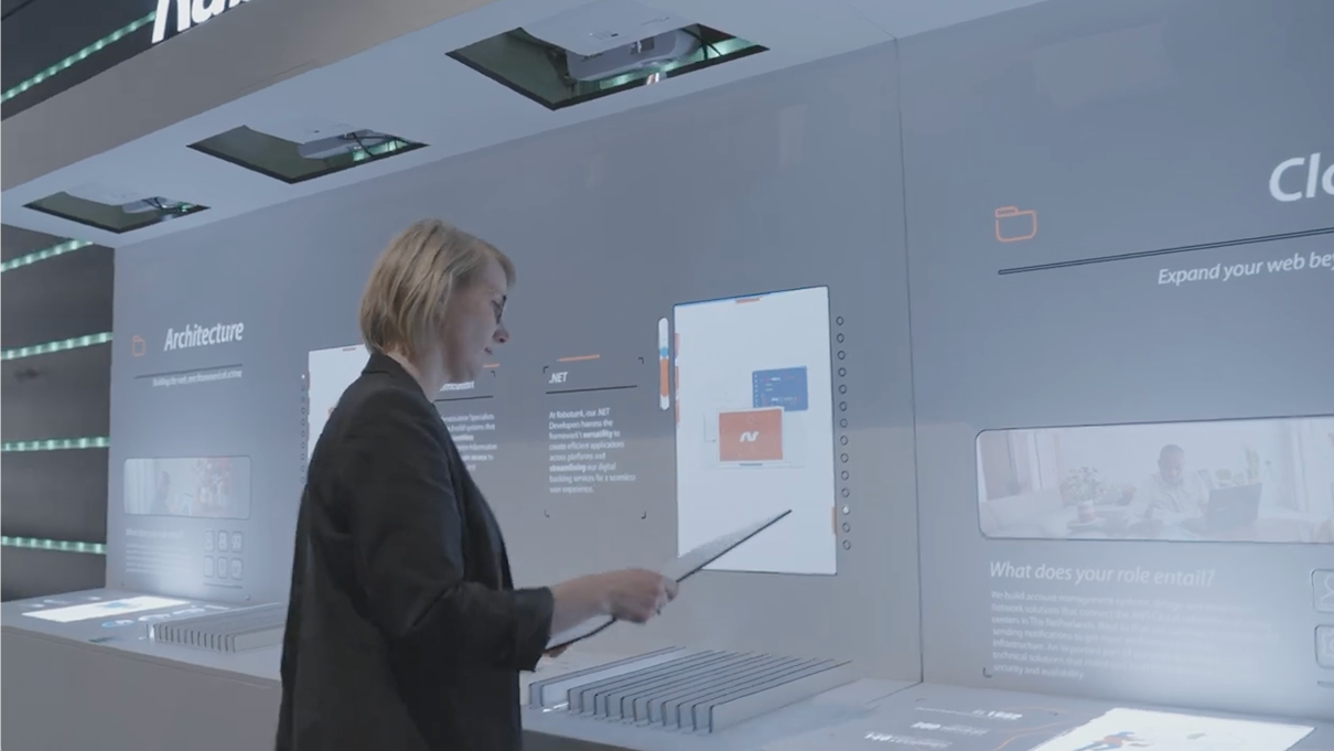 Woman interacting with a large digital interface using a stylus, showing information about software architecture.