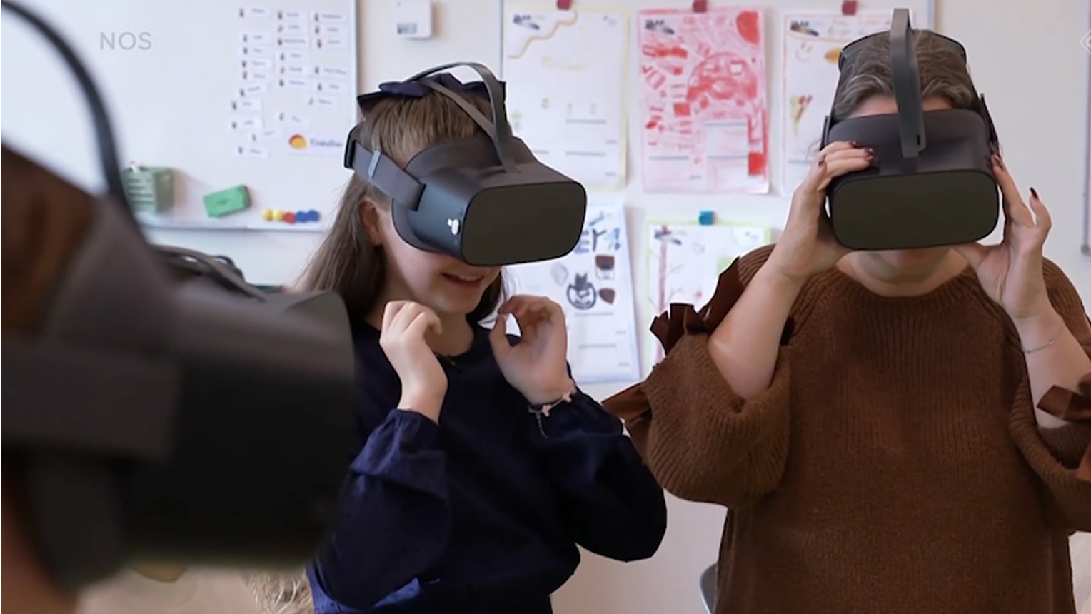 Two primary school pupils in a classroom wearing VR headsets while exploring a virtual experience, with posters and learning materials visible in the background.